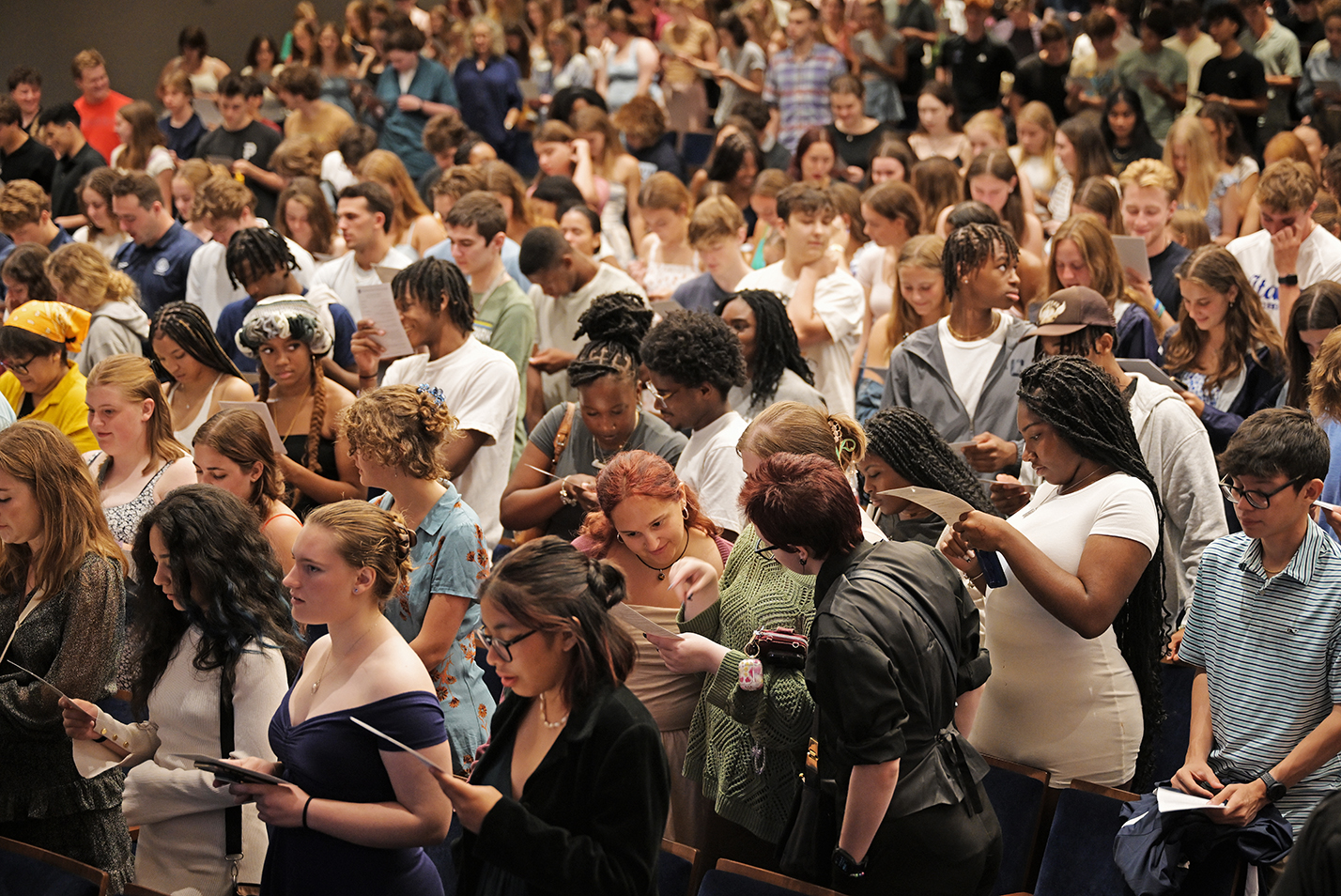 A crowd of students in an auditorium read from their programs.