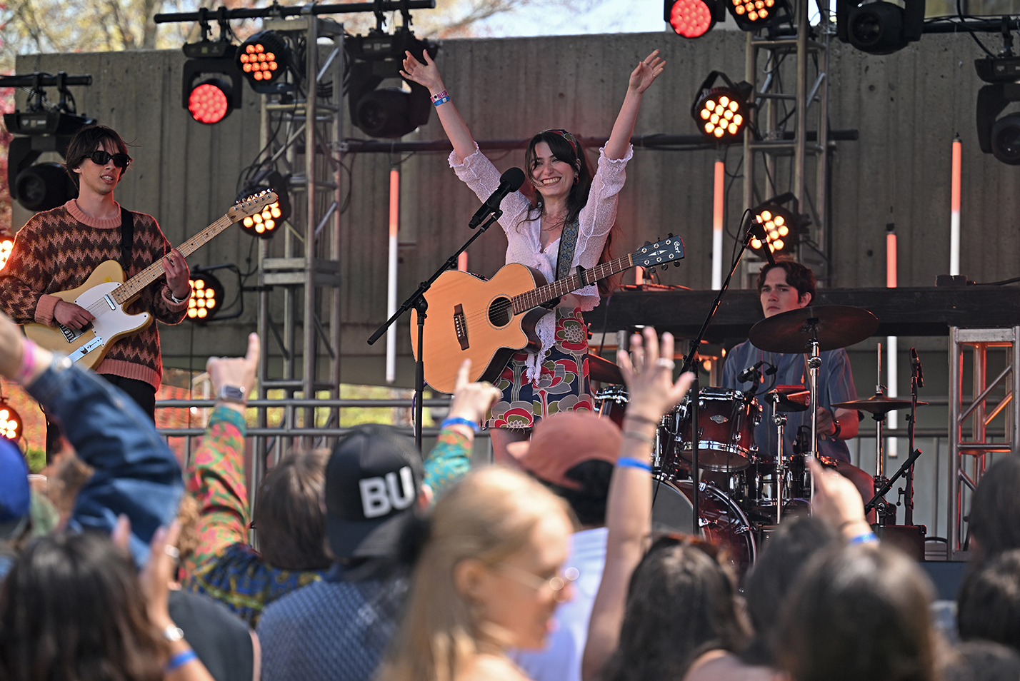 A singer with acoustic guitar raises her arms to acknowledge the applause from the audience