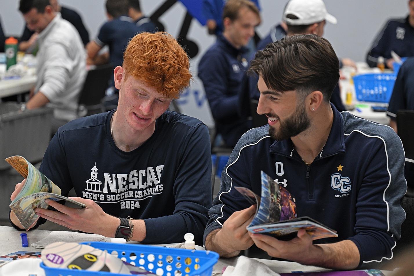 Two soccer players look at children's books during a public service event.