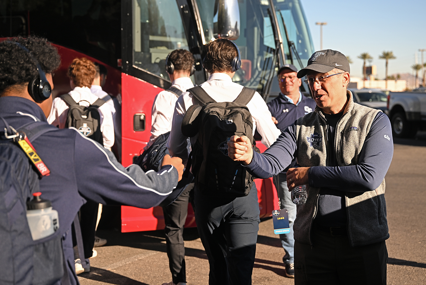 A college administrator offers encouraging fist-bump to soccer players boarding a bus to a game.