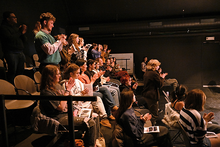 the audience stands and applauds in a black box theater