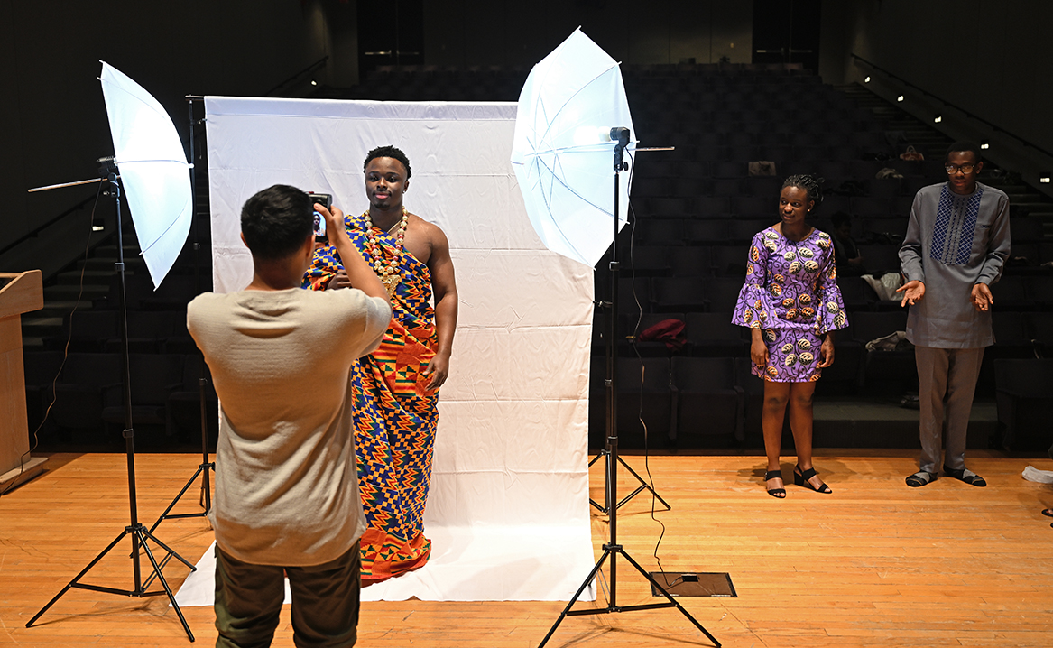 a photographer takes photos of students in ethnically inspired outfits for a fashion show