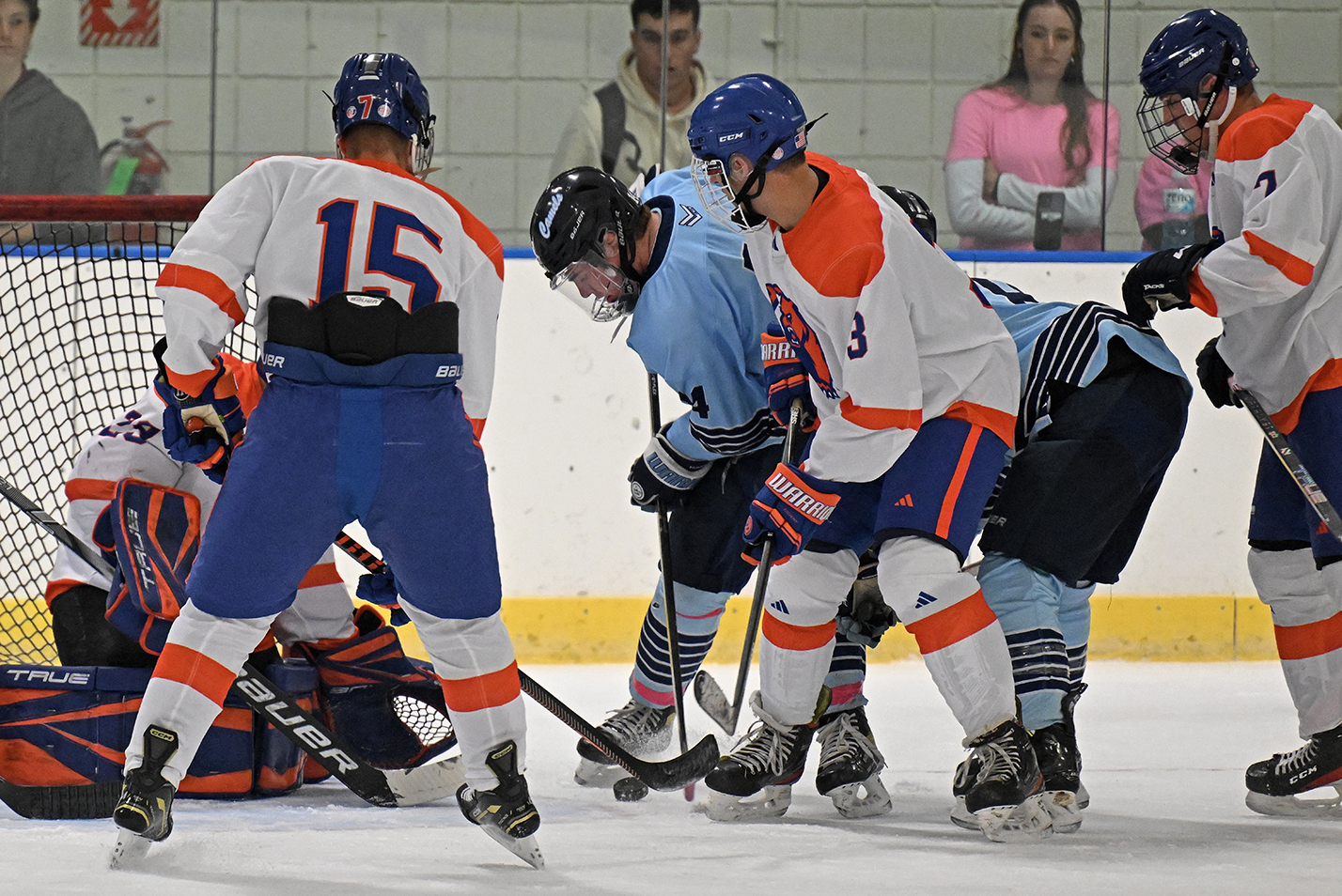 Hockey players battle for the puck in front of the goal.