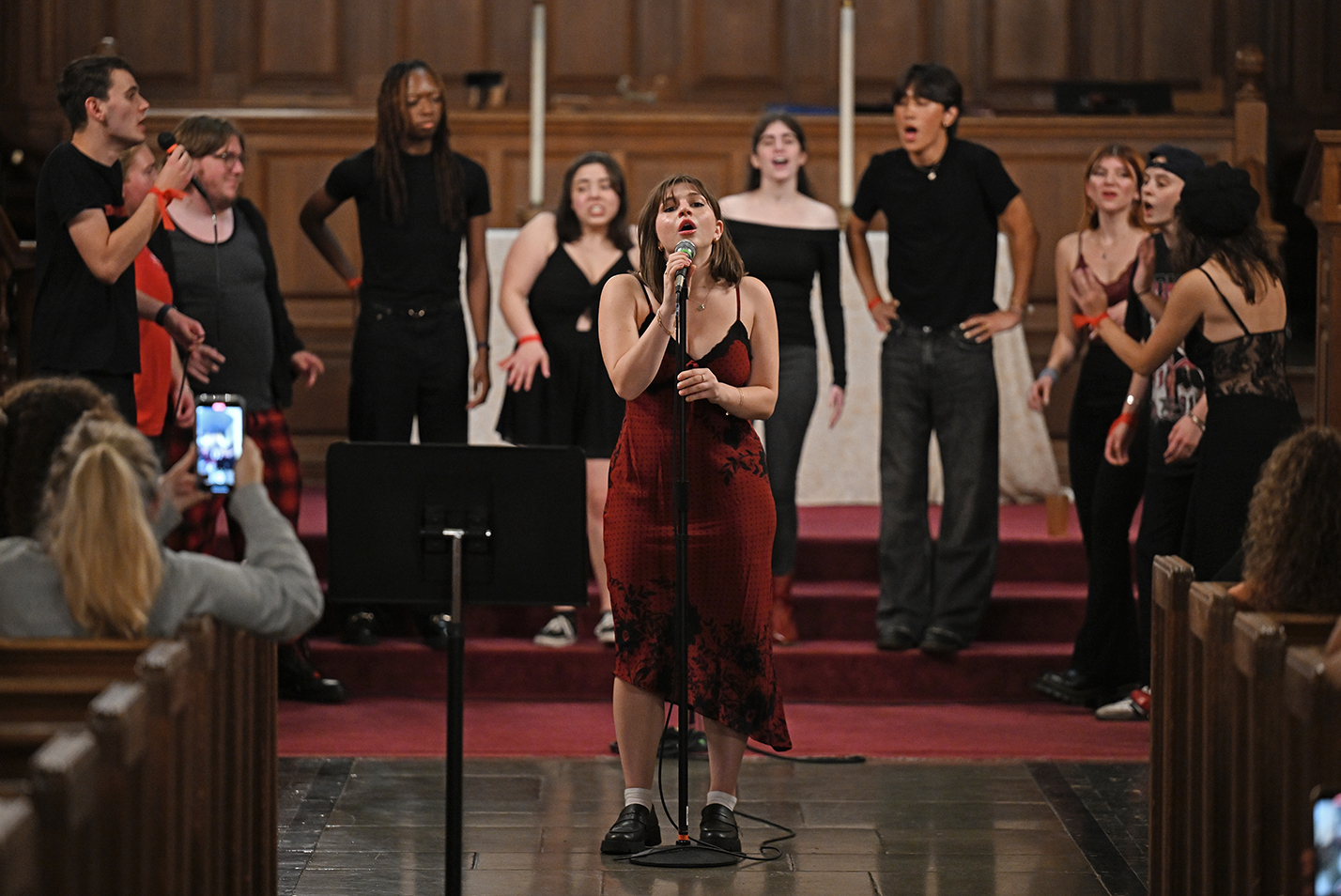 A student in a red dress solos in front of an a cappella group.